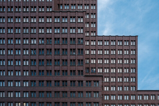 Geometric facade of a modern red brick office building with many windows against a blue sky.