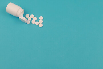 Pills spilled out of white bottle on blue background.