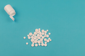 Pills spilled out of white bottle on blue background.