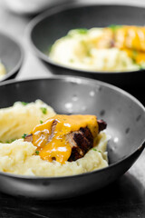 A close-up of a bowl with mashed potatoes, grilled meat, and a rich, creamy sauce, garnished with fresh herbs. The dish is beautifully presented, making it look delicious and appetizing.