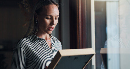 Woman, photo frame and sad by window with memory, mourning and regret or loss of loved one at home....