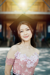 Close up of a proud Southeast Asian female graduate in traditional dress and looking at the camera in front of the modern campus building