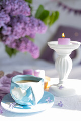 a cup with a hot drink. Breakfast with waffles and cakes, a bouquet of lilacs in a wicker basket