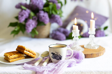 a cup with a hot drink. Breakfast with waffles and cakes, a bouquet of lilacs in a wicker basket