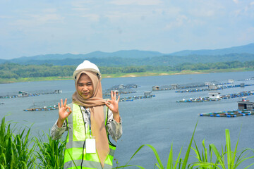 A female fish farm manager wears a safety vest and carries a book to check the work.