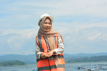 A female fish farm manager wears a safety vest and carries a book to check the work.