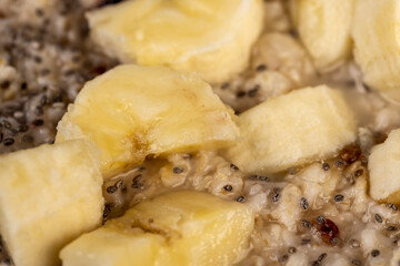 add ripe banana to quickly cooked oatmeal porridge, boiled oatmeal porridge with chia seeds, berries and fresh banana, close up