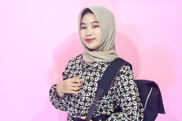 Portrait of a muslim schoolgirl carrying books in her hands and wearing a black backpack on an isolated background