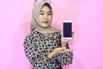 Young Asian Muslim woman who looks happy while holding a smartphone, in a casual style