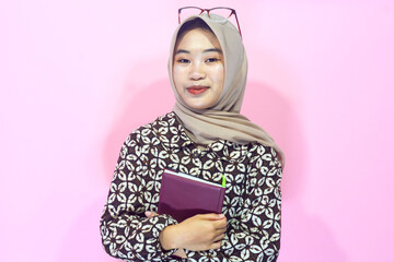 Portrait of a muslim schoolgirl carrying books in her hands and wearing a black backpack on an isolated background