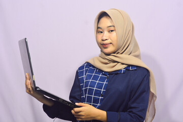 Portrait of a smart-faced Muslim female student wearing glasses, holding her laptop
