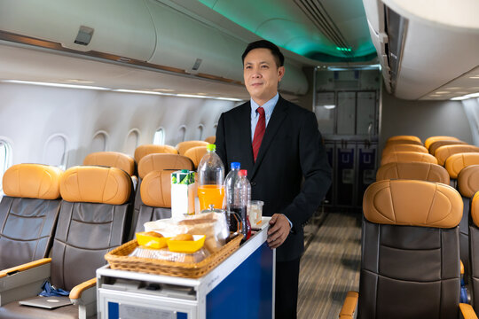 serving drinks : Portrait Stewardess holding water bottle in airplane cabin. Asian male steward serving glass of water for passengers on board. Flight attendant  and Cart on airplane