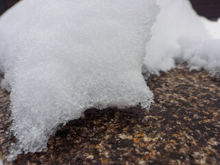 Close-up of fresh snow resting on a textured rock surface, capturing the intricate detail of icy crystals. Perfect natural winter texture for backgrounds or seasonal designs.