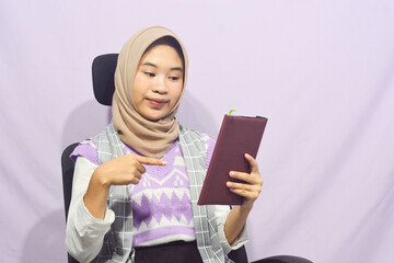 Portrait of a muslim schoolgirl carrying books in her hands and wearing a black backpack on an isolated background