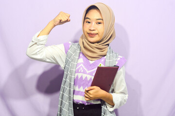 Portrait of a muslim schoolgirl carrying books in her hands and wearing a black backpack on an isolated background