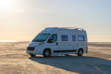 A tranquil sunset casts a warm glow over a spacious camper van parked on the scenic shores of Lakolk Strand, Romo Denmark. The tranquil beach setting invites exploration and adventure.