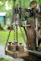 Close-up of an old, weathered weighing scale with its rusty chains and heavy metal weights, set against a blurred natural background