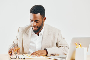 Professional young African American man working at desk with laptop and notebook in bright office,...