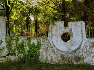 Framed by greenery, an old, weathered wall showcases circular architectural details. The structure...