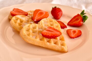 Soft heart-shaped Belgian waffles with fresh strawberries and condensed milk. Sweet and romantic breakfast for Valentine's Day or cozy morning.

