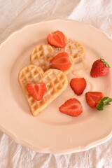 Heart-shaped Belgian waffles with strawberries and condensed milk on a plate. Sweet, soft breakfast or dessert.
