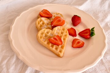 Soft heart-shaped Belgian waffles with fresh strawberries and condensed milk. Sweet and romantic breakfast for Valentine's Day or cozy morning.