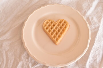 Heart-shaped waffle served on a white plate. Cute and cozy food, perfect for a romantic breakfast or Valentine’s Day.