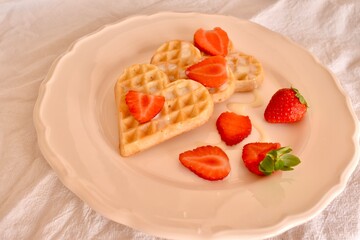 Soft heart-shaped Belgian waffles with fresh strawberries and condensed milk. Sweet and romantic breakfast for Valentine's Day or cozy morning.