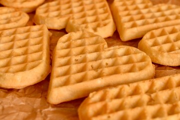 Golden heart-shaped waffles aligned on parchment paper. Warm tones, soft texture, overhead food composition.

