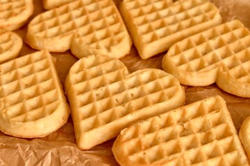 Heart-shaped Belgian waffles arranged in a row on parchment paper. Fresh, soft, golden — perfect for breakfast or dessert.