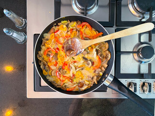 A skillet on a stovetop holds a vibrant stir-fry with sliced bell peppers, mushrooms, onions, and assorted vegetables cooking.
