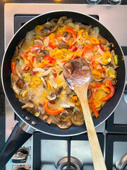 A skillet on a stovetop holds a vibrant stir-fry with sliced bell peppers, mushrooms, onions, and assorted vegetables cooking.