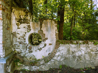 Framed by greenery, an old, weathered wall showcases circular architectural details. The structure...