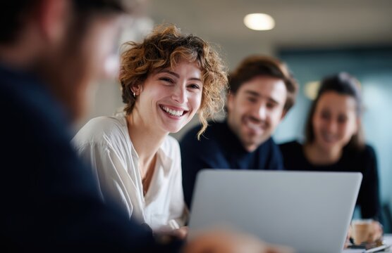 Happy young business people working together in modern office environment, collaborating and sharing ideas while using laptop. Their expressions reflect enthusiasm and teamwork
