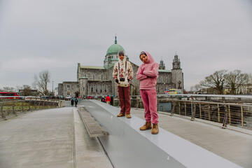 Obraz premium Ireland and Irish Countryside: Two young boys are posing on a bridge over the River Corrib with the Galway Cathedral in the background