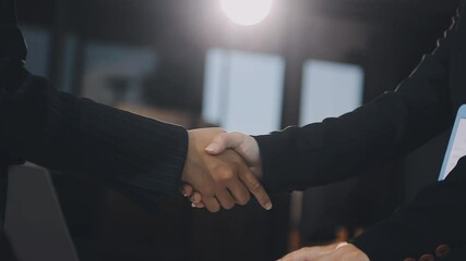 Two businessmen are firmly shaking hands across a table in a formal setting - Powered by Adobe