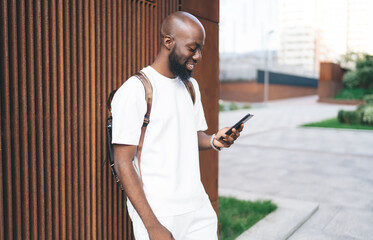 Relaxed man smiling at smartphone screen outdoors, reflecting joy from digital interaction, app experience, or message, in vibrant blend of real life and mobile connection.