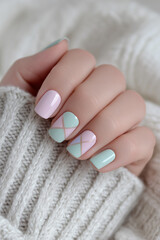 Creative nail art showcases pastel shades and geometric patterns while resting on a cozy knit sweater