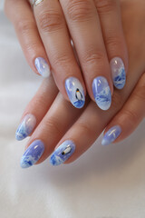 Elegant blue nail art featuring a winter landscape and a charming penguin in a serene setting