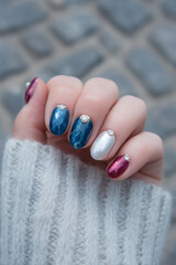 Naklejka premium Creative nail art featuring a glossy blue, silver, and pink design on an inviting hand during a cozy autumn afternoon