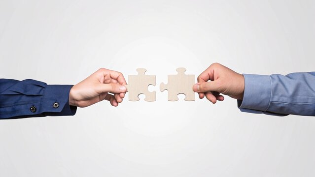 Two hands holding wooden puzzle pieces that fit together, symbolizing cooperation and problem-solving