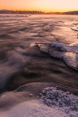 Stunning winter sunset over a frozen river in Norway with ice formations and mist