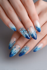 Elegant blue ombre nails adorned with sparkling crystals showcase a glamorous manicure in a serene setting