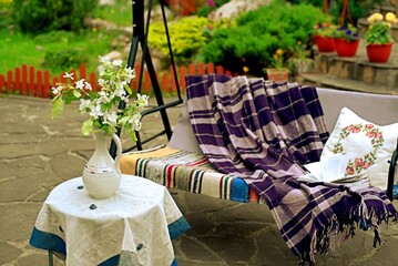 Apple blossoms on a table in front of a sofa swing in the courtyard of a country house.