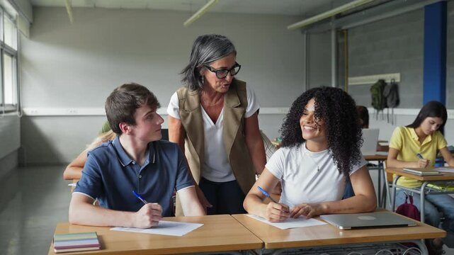 Mature female teacher helping teenager students learning writing text at College High School