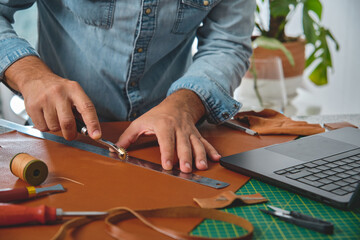 Craftsman using stitching groover and ruler on leather in his workshop, small business and...