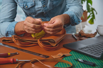 Obraz premium Leather craftsman carefully stitching a handmade bag in his workshop, surrounded by tools and technology