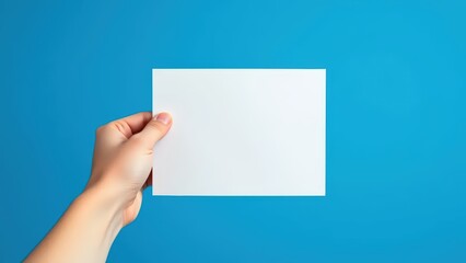 Fototapeta premium hand holding a blank white sheet of paper on a solid blue background