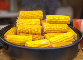 Freshly cooked corn on the cob steaming in a large pot. Bright yellow corn stacked high, ready to be served at a market or food stall. Tasty and healthy street food snack.