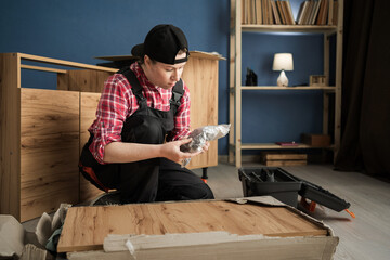Handyman with parts of new furniture, metal screws and tools for furniture assembly on the floor.